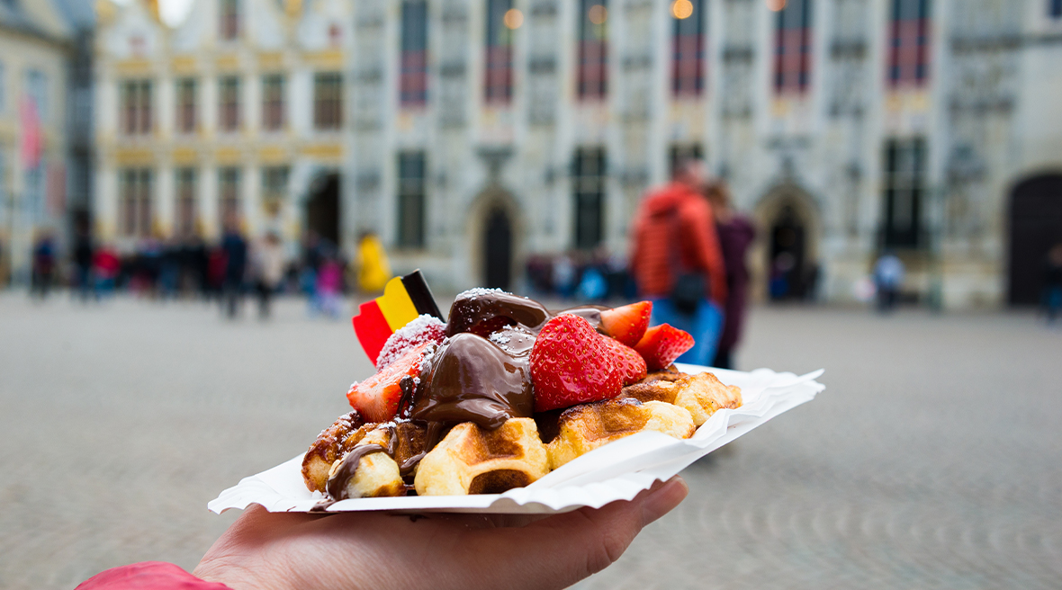 Belgium waffle with chocolate sauce and strawberries with a Belgian flag with Bruges city in the background
